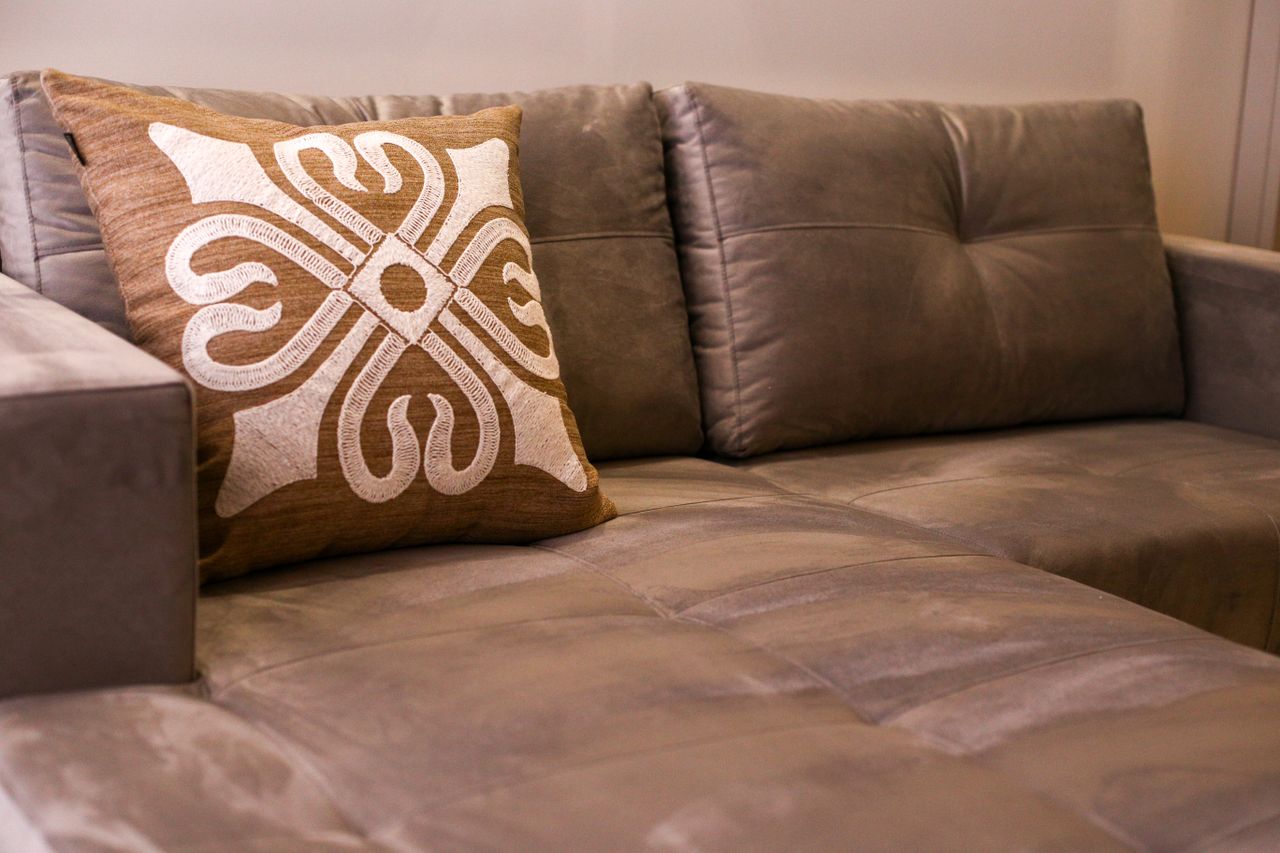 about-us A close-up of an elegant gray sofa with an artistic decorative cushion in a modern living room.