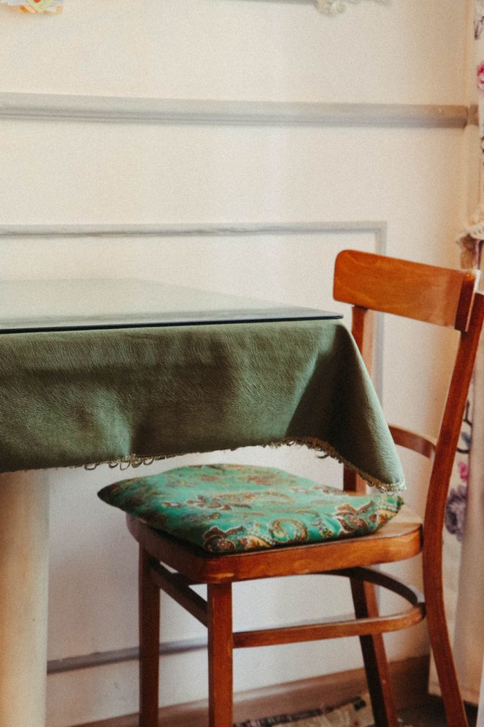 Warm and inviting home interior featuring a wooden chair with a cushion and a table draped in a green tablecloth.