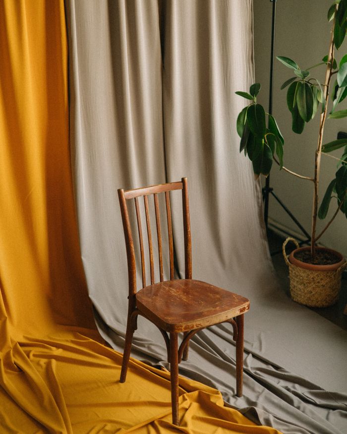 Vintage wooden chair with potted plant and draped fabric creating an artistic indoor scene.