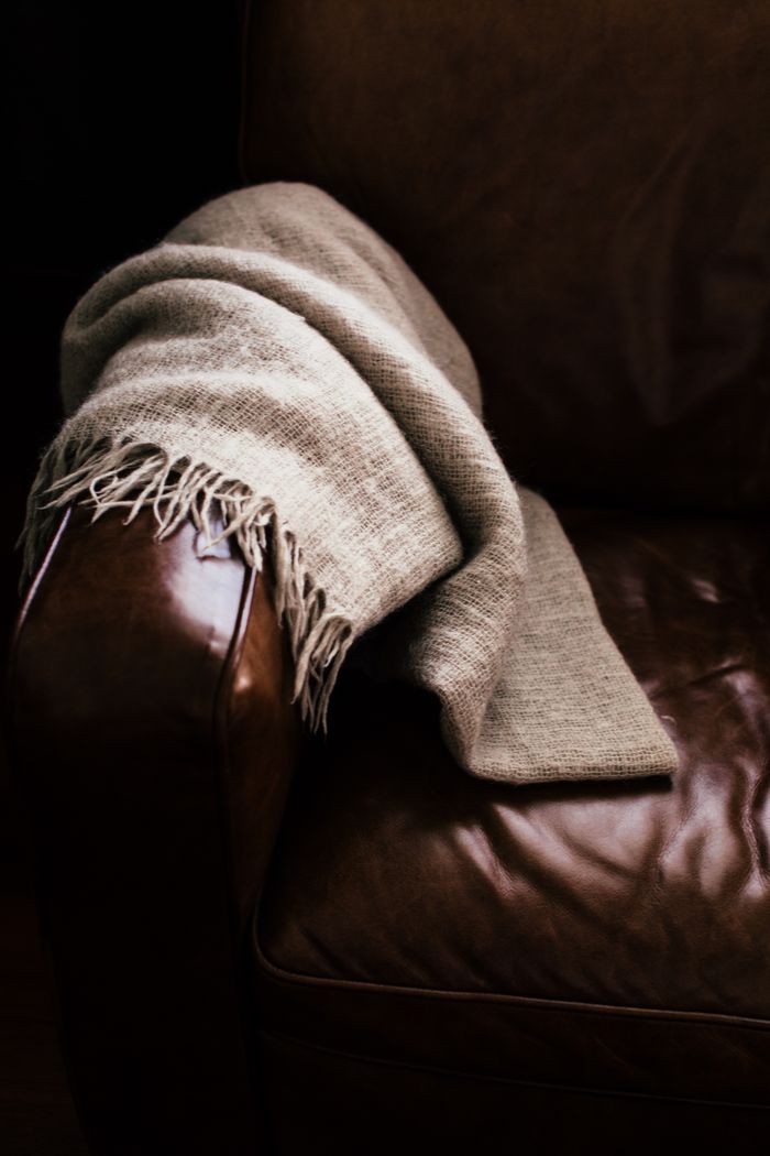 Warm beige scarf draped over dark brown leather arm indoors, offering a cozy and inviting atmosphere.