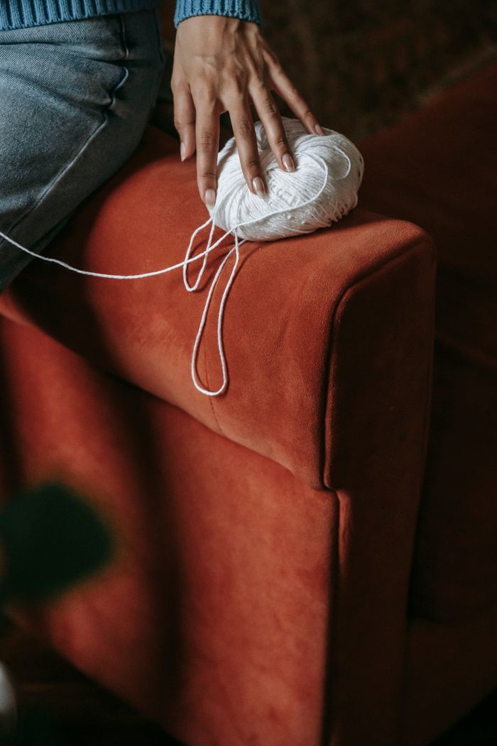 services-06 A hand resting on a soft orange couch holding a skein of white yarn indoors.